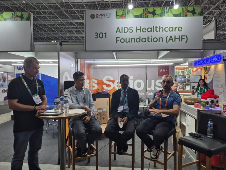 Panel discussion at a trade show booth for AIDS Healthcare Foundation (AHF), booth number 301, with four men seated and one speaking into a microphone.