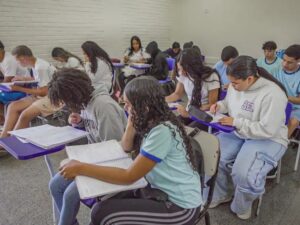 Students in a classroom seated at purple desks, writing in notebooks and studying.